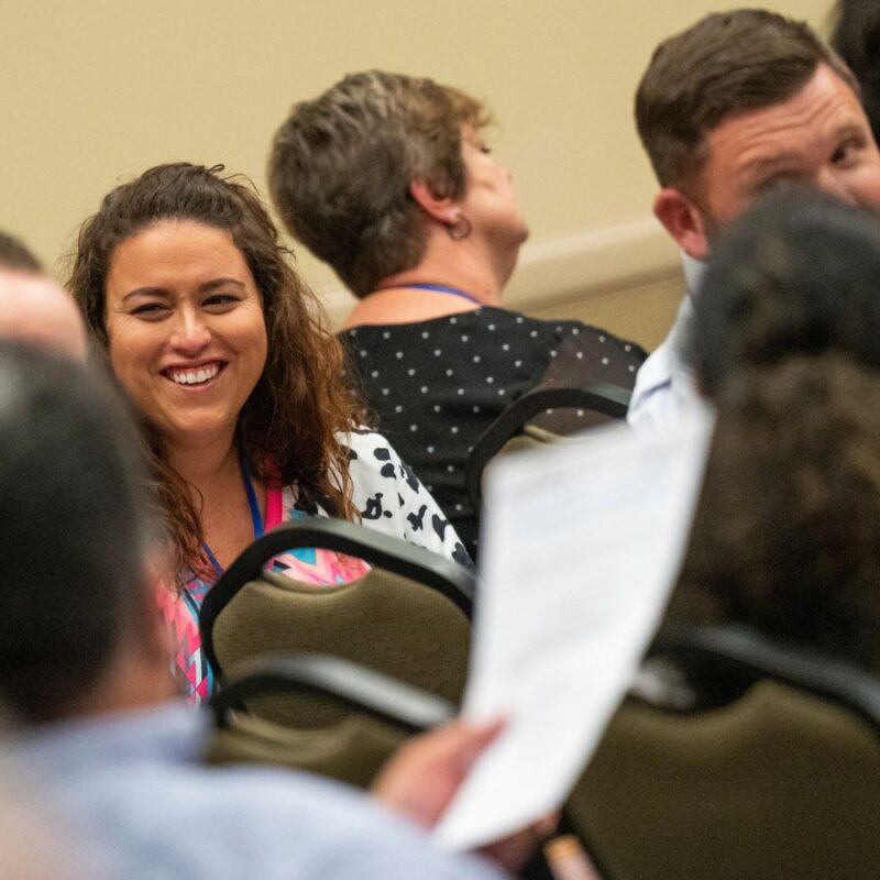 Woman smiling at colleagues in a seated crowd in a conference room