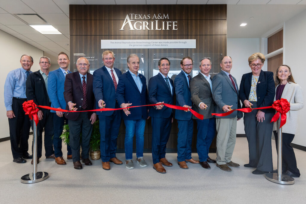 A row of people in suits cutting a ribbon in front of a wood-panel wall showing the names of donors